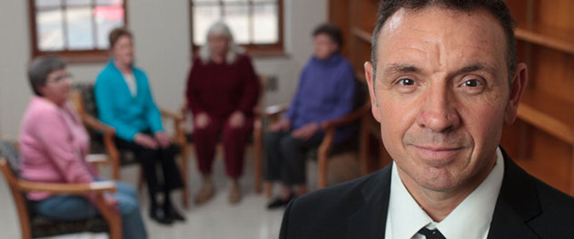 Photograph showing a close up of Dr. Benzo with people seated in a semi-circle in the background.