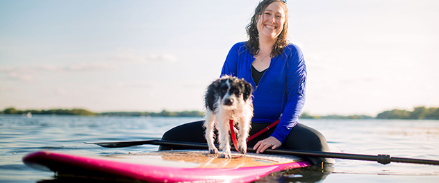 Smiling woman and dog on stand-up paddleboard