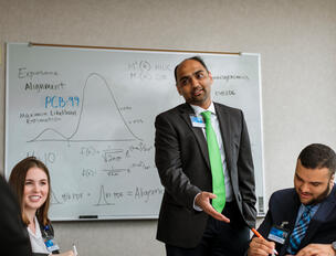 Dr. Athreya stands in front of a whiteboard addressing lab members.