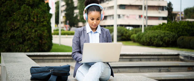 Young professional woman using laptop and headphones in city park