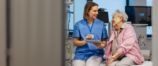 A nurse holding a tablet and talking to patient in a hospital room