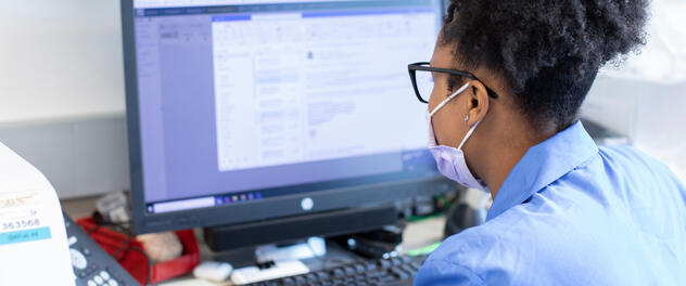 A person wearing a mask and looking at a computer screen