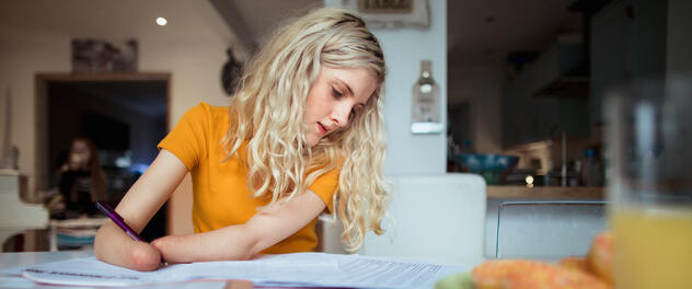 A young girl with limb differences of both arms holds a pen while doing schoolwork